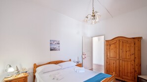 Un dormitorio con cama de madera, una mesita de noche con lámpara, un armario y una puerta que da a otra habitación.