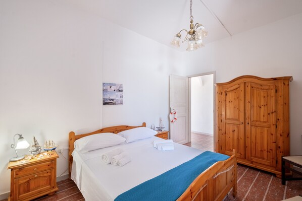 Un dormitorio con cama de madera, una mesita de noche con lámpara, un armario y una puerta que da a otra habitación.