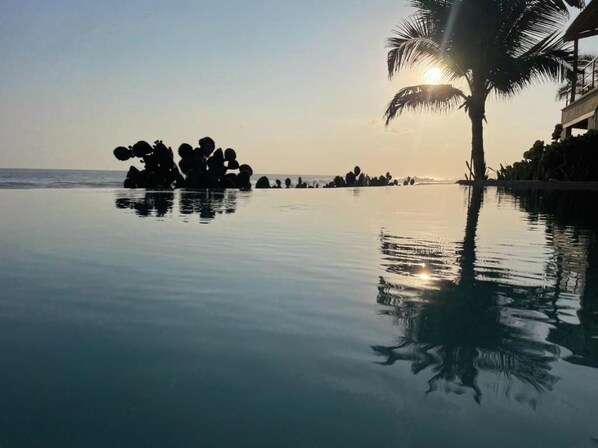 A serene pool area with a clear view of the ocean and a palm tree silhouette.