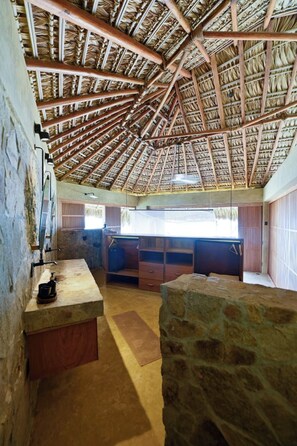 A room with a thatched roof, stone walls, a wooden counter, and a window with a view.