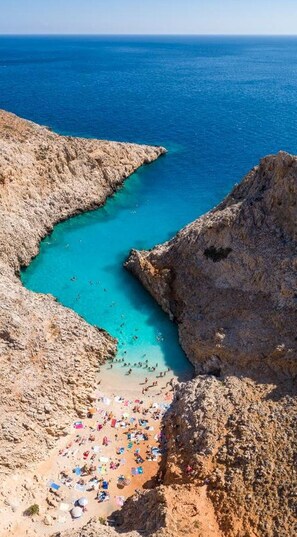 A coastal landscape with a rocky beach, clear turquoise waters, and a view of the sea.
