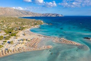 An aerial view of a coastal area with a beach, clear blue waters, and a mountainous backdrop. - Villa Erofili in Agia Triada (Rethymno)