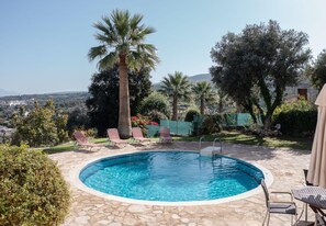 A swimming pool with a stone deck, surrounded by palm trees and lounge chairs.
