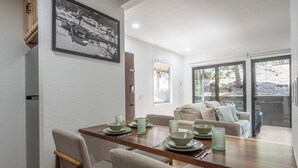 Un coin repas avec une table en bois dressée pour quatre personnes, un canapé et un tableau encadré au mur.