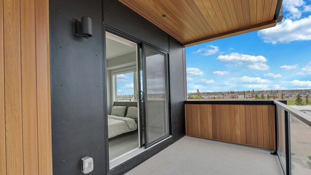 En moderne balkon med træloft, store skydedøre ind til et soveværelse og udsigt over bybilledet.