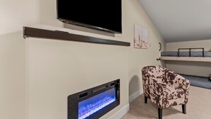 A room with a TV mounted on the wall, a built-in aquarium, a patterned armchair, and a bunk bed with a mattress on the floor.