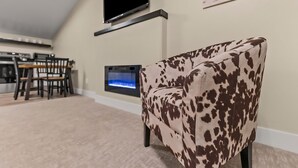 A living room with a sofa, a flat-screen TV mounted on the wall, a fireplace, and a dining area with chairs and a table.