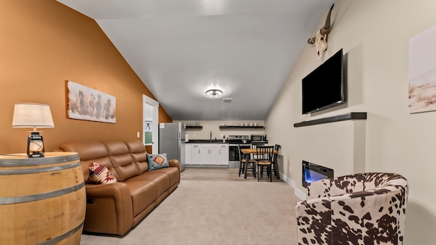 A modern living room with a brown leather sofa, a wooden barrel, and a cow print armchair. A flat-screen TV is mounted on the wall, and a dining area is visible in the background.