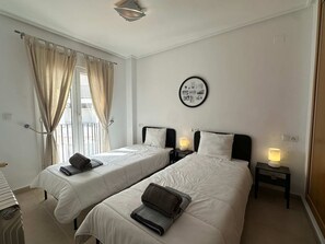 Une chambre d’hôtel avec deux lits, une table de chevet avec une lampe, une fenêtre avec des rideaux et un tableau accroché au mur.