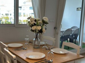 A dining table set for four with white plates, cutlery, and a vase of white flowers.