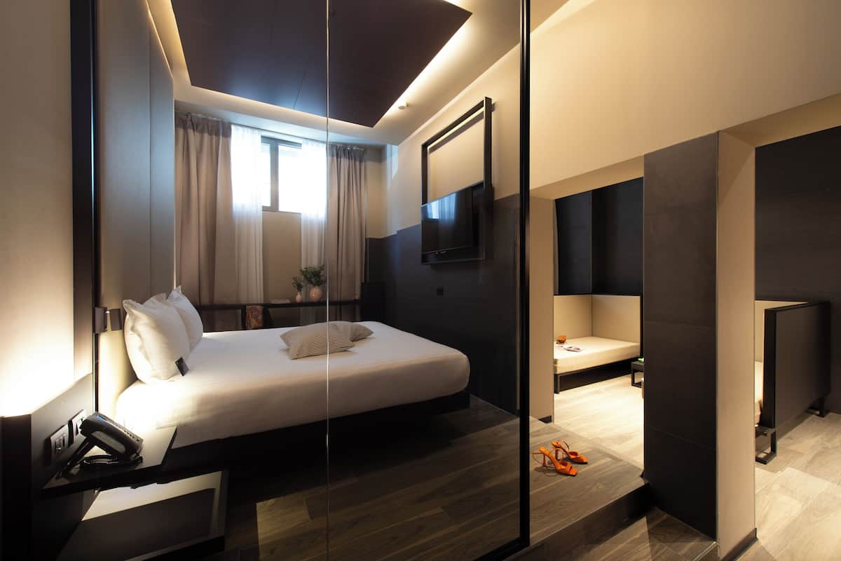 A modern hotel room with a large bed, a TV mounted on the wall, a bedside table with a phone, and a small seating area with a sofa and a table.