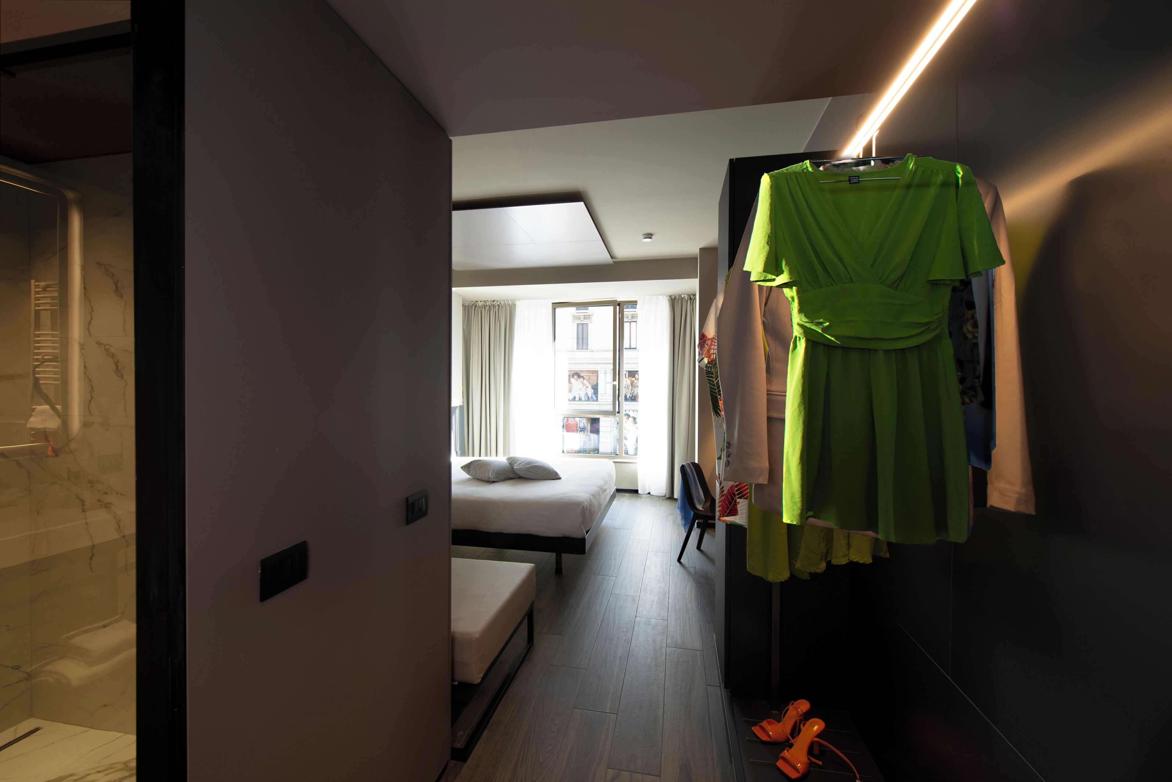 Une chambre d’hôtel avec un lit, un petit bureau et une robe vert vif accrochée au mur.