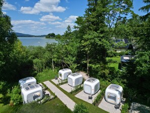 A row of modern, white, cube-shaped mobile homes with large windows, arranged in a grassy area with a lake and trees in the background. - Directly on Lake Wallersee - Cubes - SELF CHECK-IN (Henndorf am Wallersee)