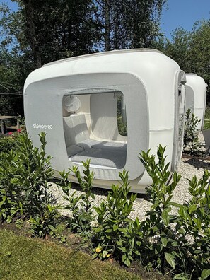 A white sleeperco with a window and a door, surrounded by greenery. - Directly on Lake Wallersee - Cubes - SELF CHECK-IN (Henndorf am Wallersee)