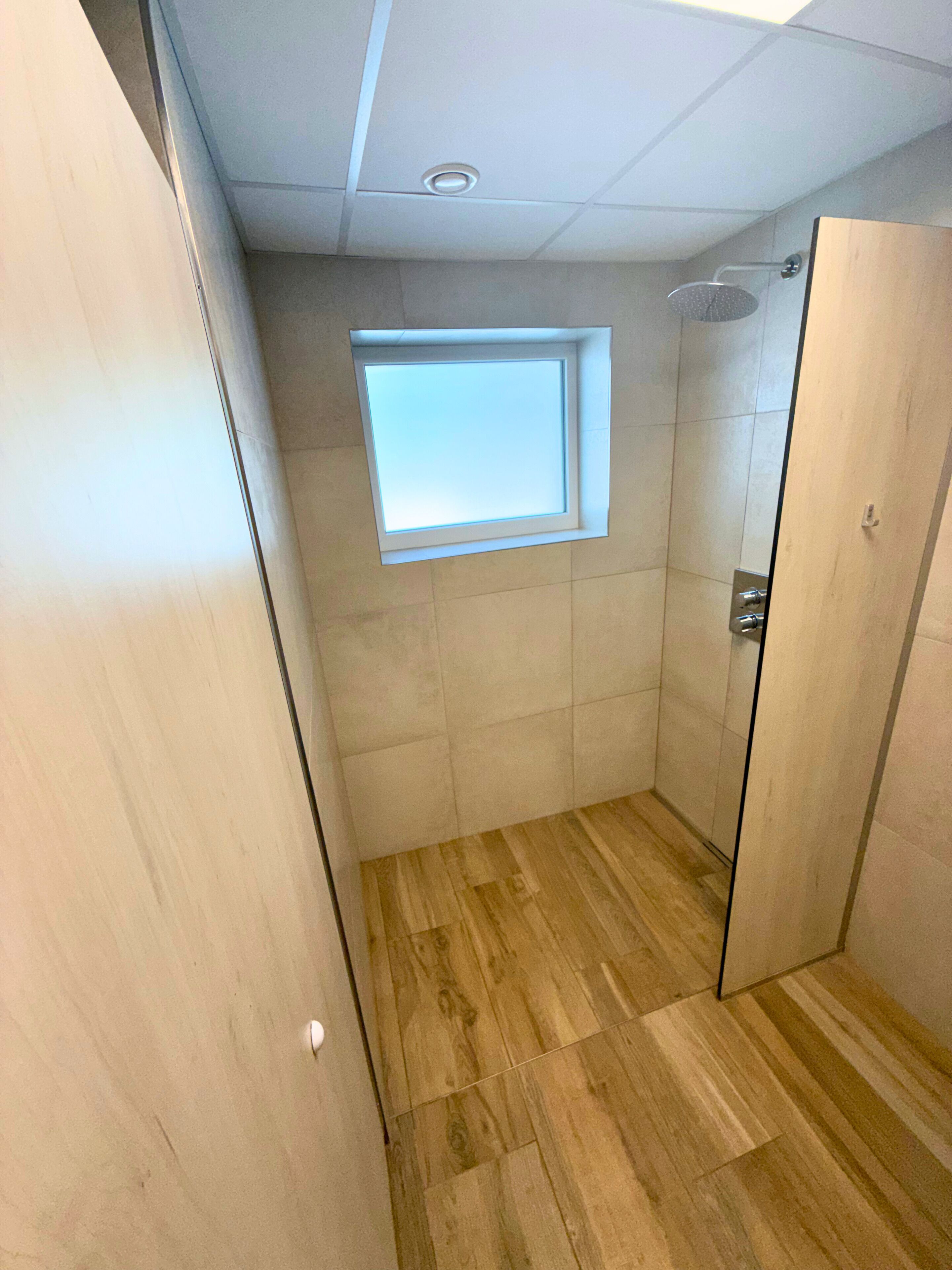 A modern bathroom with a wooden floor, a window, and a shower.