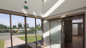 A modern building entrance with large glass doors, a visible emergency exit sign, and a view of a parking area with a vehicle. - Directly on Lake Wallersee - Cubes - SELF CHECK-IN (Henndorf am Wallersee)
