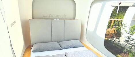 Ein kompakter, moderner Schlafraum mit Bett, Kopfstütze und Fenster mit Blick auf Grünflächen.