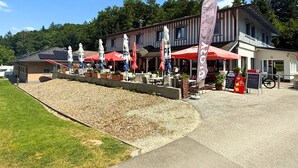 An outdoor seating area with tables and umbrellas, a building with a sloped roof, and a flag with the text "GloryBowl". - Directly on Lake Wallersee - Cubes - SELF CHECK-IN (Henndorf am Wallersee)