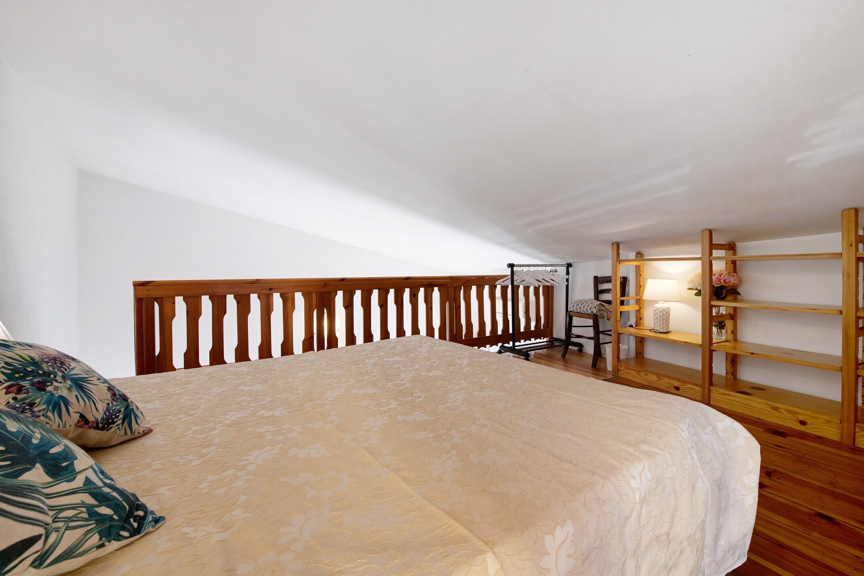 Una camera da letto con un letto, una testiera in legno, una sedia, uno scaffale e una lampada.