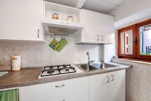Une cuisine équipée d’une cuisinière à gaz, d’un évier, de meubles blancs et d’une fenêtre donnant sur un beau paysage.
