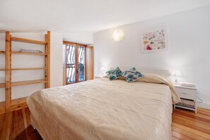 Une chambre à coucher avec un lit, une échelle en bois, une table de chevet, des œuvres d’art murales et une fenêtre donnant sur un paysage.