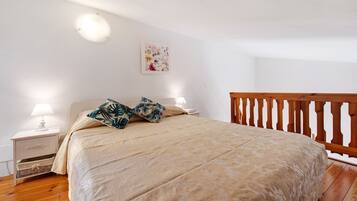 A bedroom with a bed, nightstands, a lamp, a wooden railing, and a floral wall decoration.