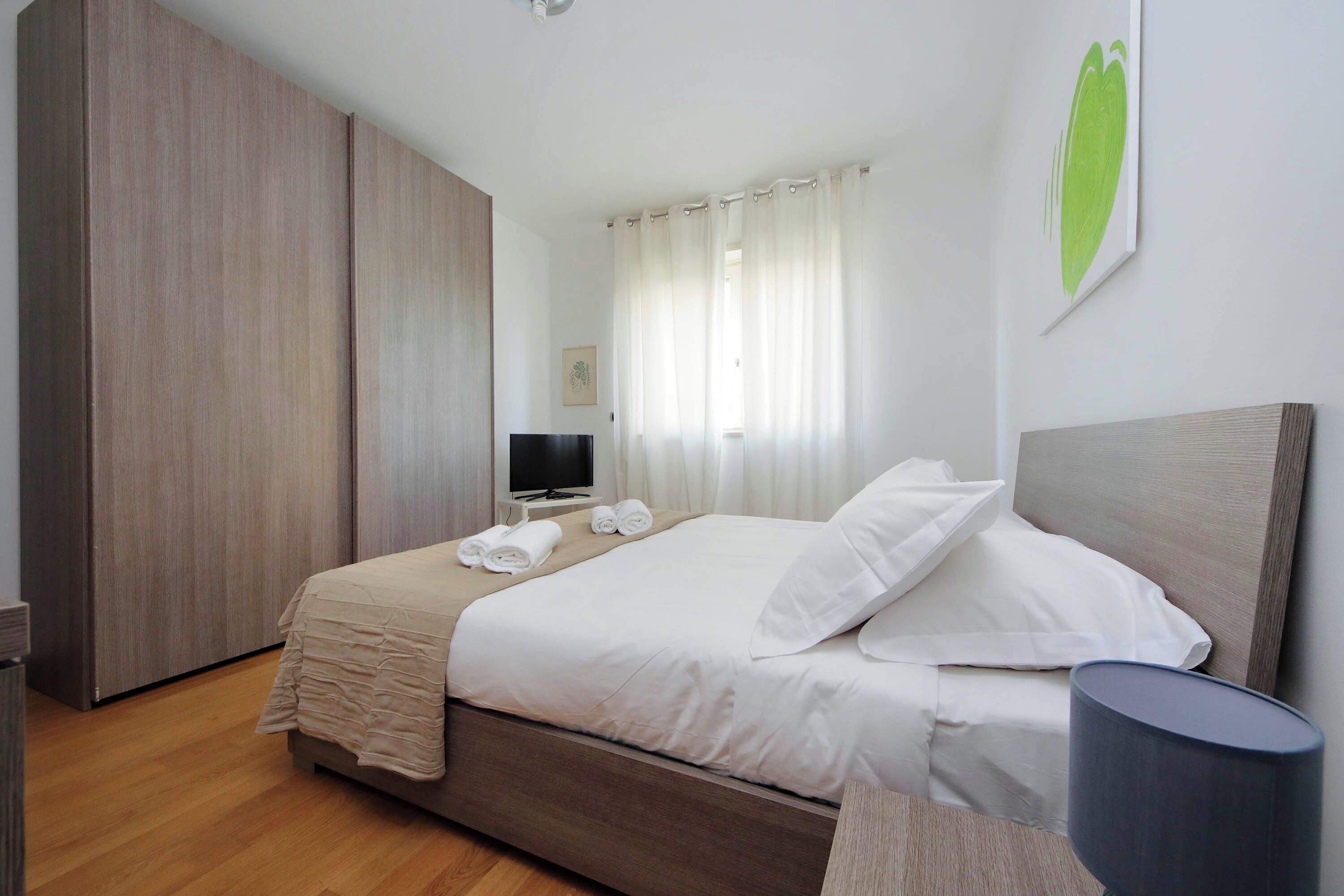 Una habitación de hotel moderna con una cama grande, un televisor de pantalla plana y un armario.