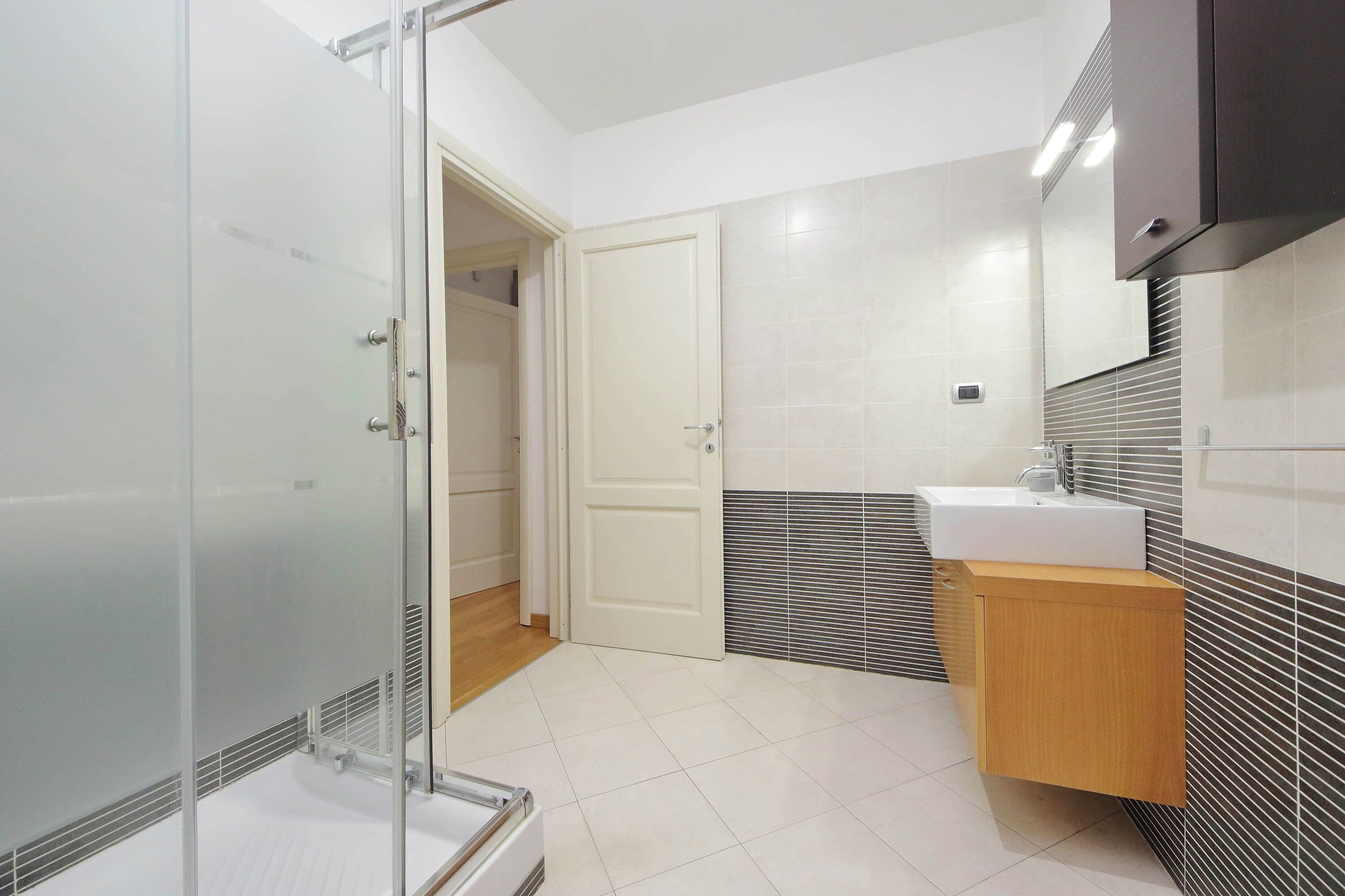A modern bathroom with a glass shower enclosure, a white sink, and a wooden vanity.