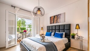 Un dormitorio con cama, mesita de noche, lámpara, planta en maceta y vistas al exterior.