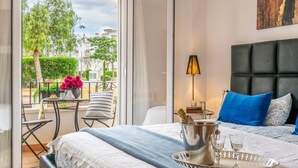 Un dormitorio con cama, una mesita de noche con lámpara, una bandeja con vasos y vistas al exterior.