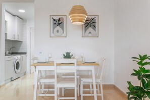 A dining area with a wooden table, white chairs, and a hanging pendant light. - ‘Loleta’ Vacation Apartment with Pool, Slides, Private Terrace & Wi-Fi (Corralejo)