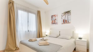 Habitación de hotel con una cama, dos mesitas de noche, cortinas y dos obras de arte en la pared.