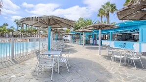 Un área junto a la piscina con mobiliario exterior, sombrillas y un bar.
