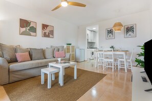 A living room with a sofa, coffee table, and a dining area with a table and chairs. - ‘Loleta’ Vacation Apartment with Pool, Slides, Private Terrace & Wi-Fi (Corralejo)