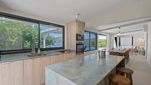 A modern kitchen with large windows, a central island, and a dining area with a view of the outdoors. - Villa Pantone - Three Bedroom Villa, Sleeps 6 (Le Robert)
