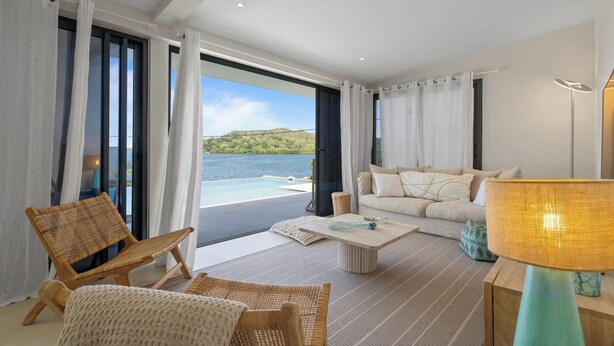 A modern living room with a view of a lake and hills, featuring wicker furniture, a sofa, and a coffee table. - Villa Pantone - Three Bedroom Villa, Sleeps 6 (Le Robert)