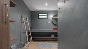 A bathroom with a wooden door, a ladder, a small window, a round mirror, and a grey patterned rug. - Villa Pantone - Three Bedroom Villa, Sleeps 6 (Le Robert)