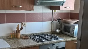 A kitchen with wooden cabinets, a gas stove, a microwave, and a refrigerator. - S+1 at Résidence Ghassen (Ariana)