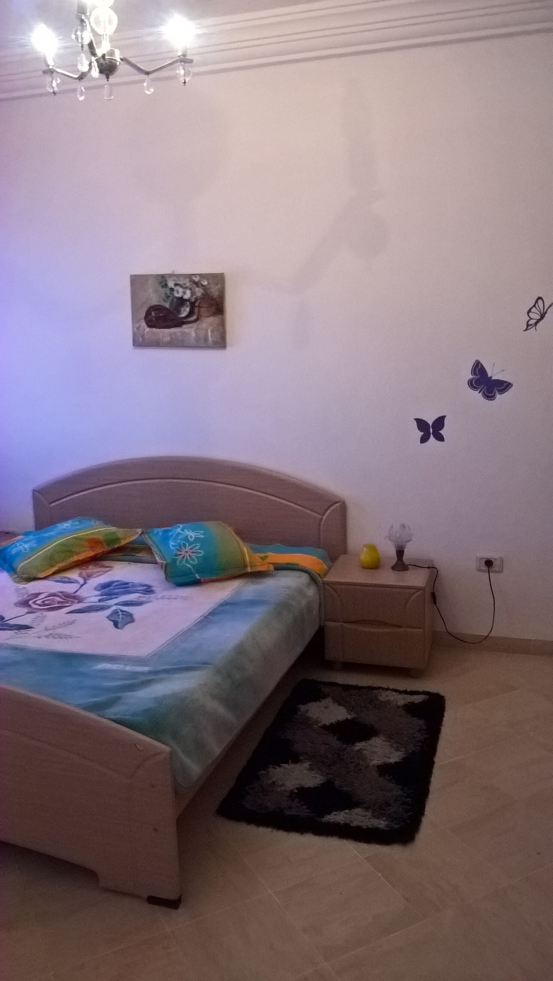 A bedroom with a bed, bedside table, and a wall-mounted light fixture.