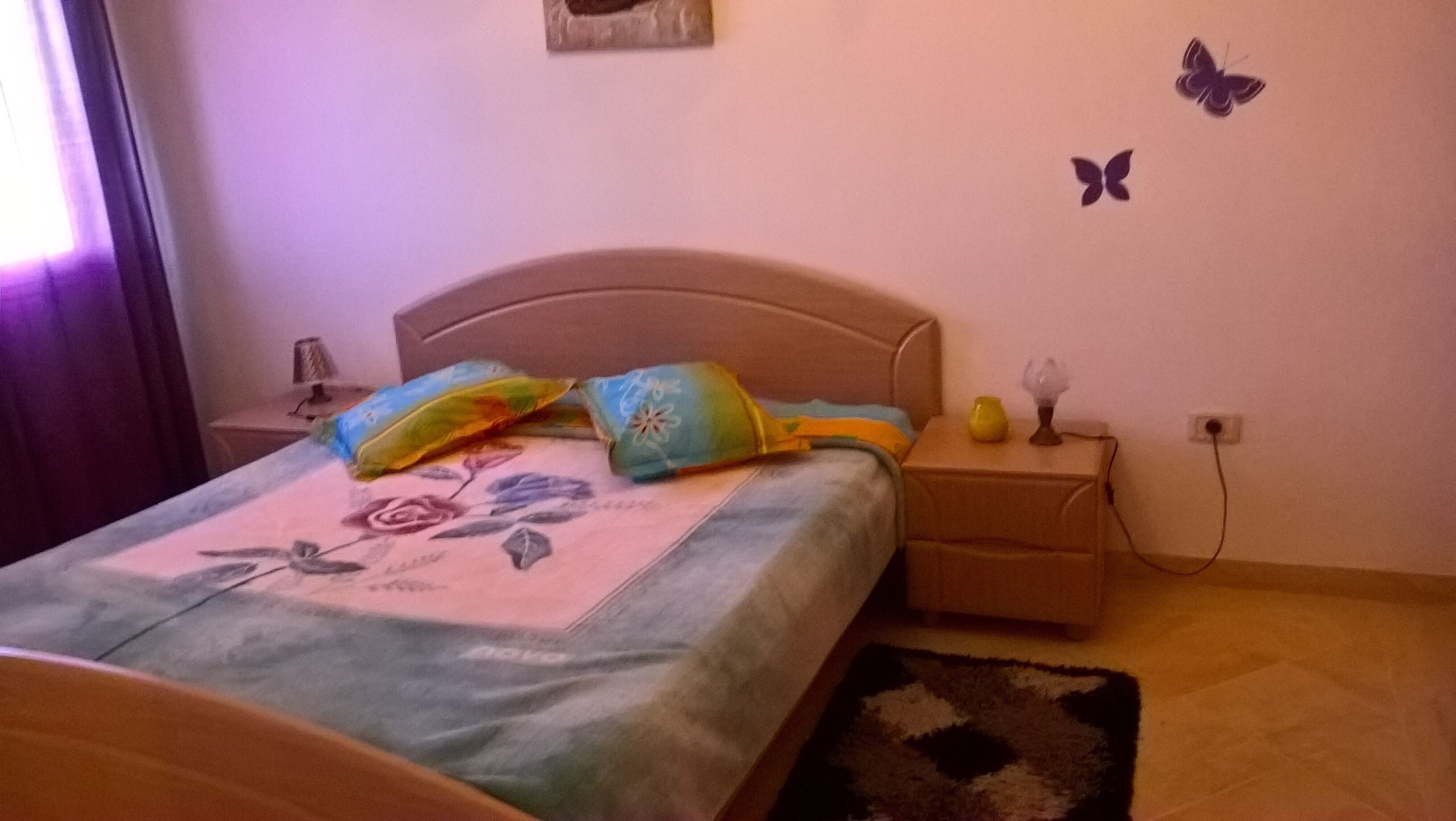 A bedroom with a bed, a nightstand, a lamp, and butterfly wall decals.