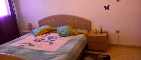 A bedroom with a bed, a nightstand, a lamp, and butterfly wall decals.