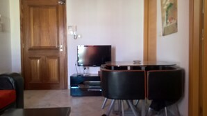 A room with a wooden door, a television, and a black table with chairs. - S+1 at Résidence Ghassen (Ariana)