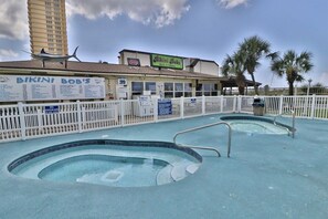 Un espace piscine entouré d’une clôture blanche, un restaurant appelé « Bikini Bob’s » en arrière-plan et un immeuble de grande hauteur.