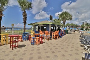 Un café situé en bord de mer, avec une terrasse et une piscine en arrière-plan.