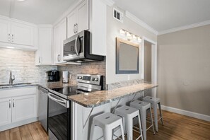 A modern kitchen with white cabinetry, a granite countertop, a built-in oven, and a microwave. There are three bar stools and a large mirror above the countertop. - 1bd 1.5ba 3rd Floor Summit Beach Front Sleeps 5 (Panama City Beach)