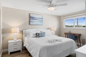 Une chambre à coucher comprenant un lit, des lampes de chevet, un ventilateur de plafond, une fenêtre avec des stores et un bureau.