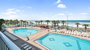 A resort with two large swimming pools, beach access, and palm trees.