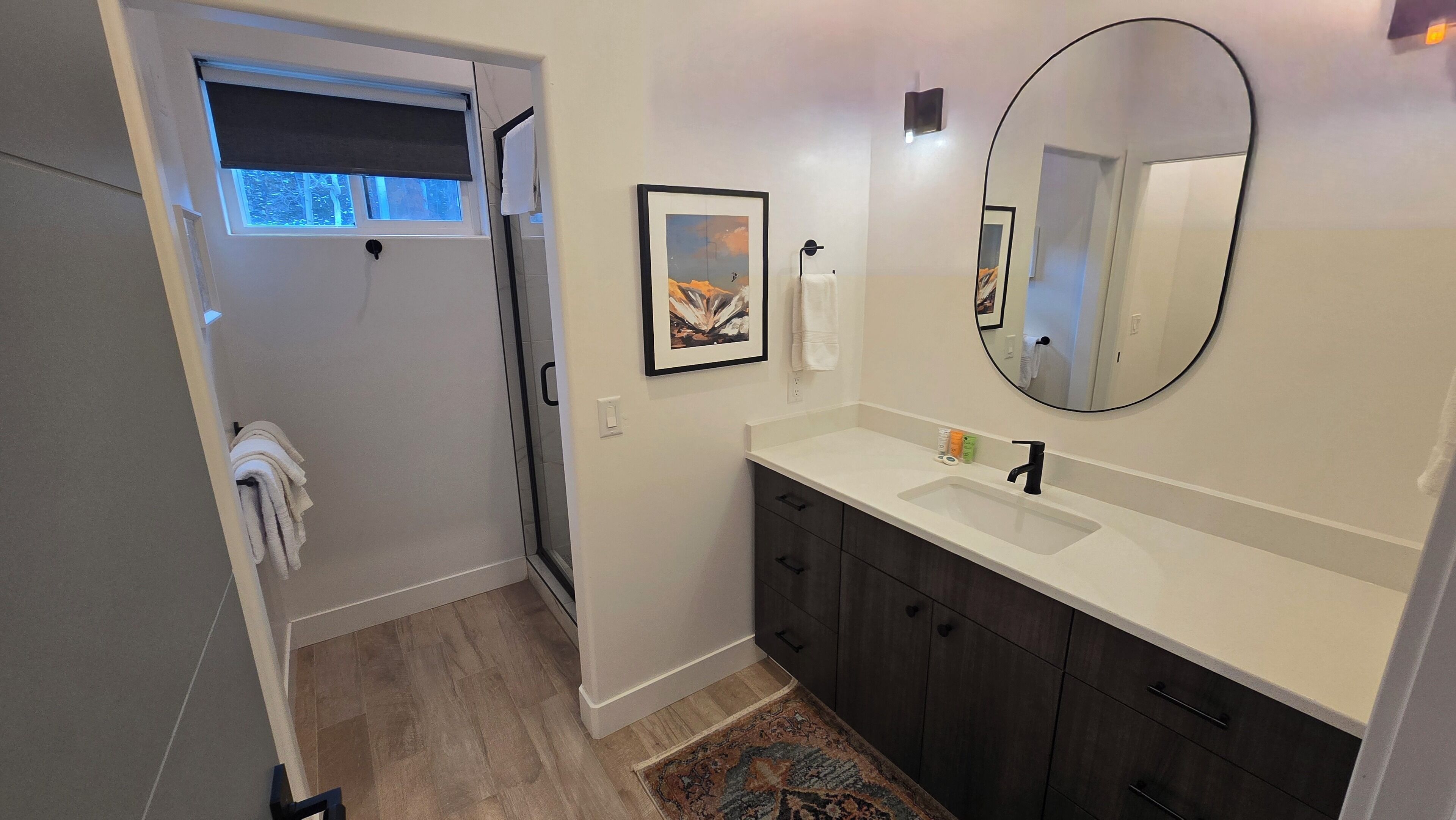 A bathroom with a white sink, dark cabinets, a large mirror, and a framed picture on the wall.