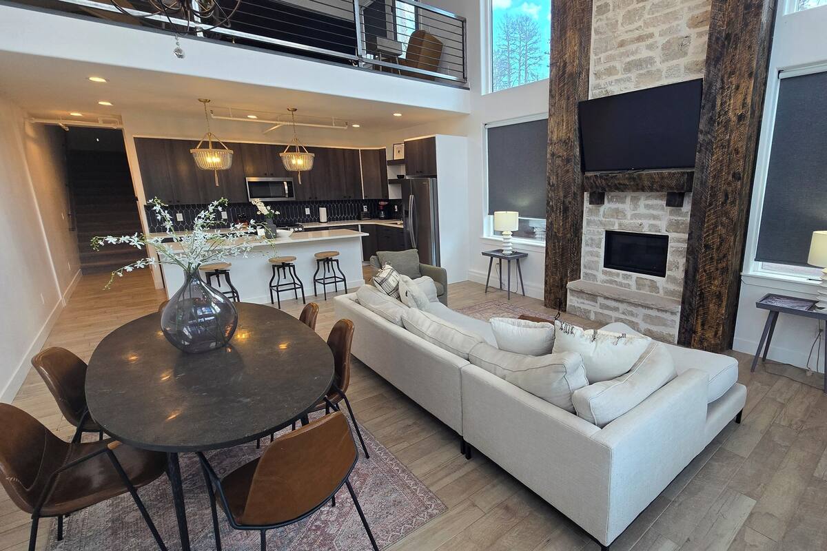 A spacious living area with a large sofa, dining table, and chairs, a kitchen in the background, and a fireplace.
