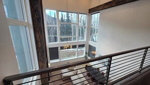 A high-ceilinged room with large windows overlooking a snowy landscape, a hanging light fixture, and a staircase with a metal railing. - Eagle Point Resort (Beaver)